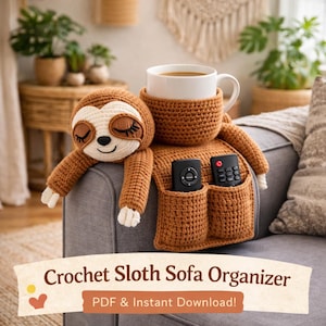 Könnte beinhalten: Ein brauner gehäkelter Faultier-Sofa-Organizer mit einer weißen Kaffeetasse. Das Faultier hat geschlossene Augen und hält eine Tasche für zwei Fernbedienungen. Der Text auf dem Banner lautet "Crochet Sloth Sofa Organizer".