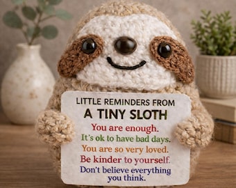 May include: A handmade crochet sloth toy with a cream-coloured face, brown details, and a smiling expression. It holds a card with the text "LITTLE REMINDERS FROM A TINY SLOTH" and positive affirmations. The text "A Tiny Pocket Hug" is at the bottom.
