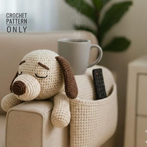 May include: A crocheted dog toy with brown ears and snout rests on a beige couch armrest. A gray mug and a remote control are also on the armrest. The text "CROCHET PATTERN ONLY" is in the upper left corner.