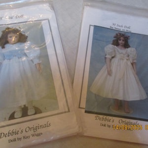 May include: Two dolls in packaging. One doll is 25-26 inches tall, wearing a white dress with blue accents. The other doll is 30 inches tall, in a white dress. Both dolls are from Debbie's Originals.