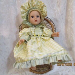 May include: A doll with blonde hair and blue eyes, wearing a yellow and white checkered dress and bonnet. The doll is seated in a small wicker chair, with a green ribbon accenting the dress and bonnet.