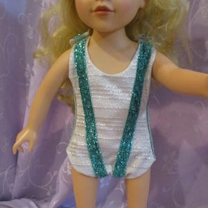 May include: A white leotard with teal glitter trim. The leotard has a scoop neck and a racerback style.