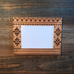 May include: A wooden picture frame with a geometric pattern carved into the border. The frame is light brown with dark brown accents.