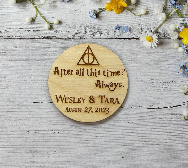 May include: A round wooden coaster with a Harry Potter themed design. It features the Deathly Hallows symbol, the text "After all this time? Always." and the names "Wesley & Tara" with the date "August 27, 2023".
