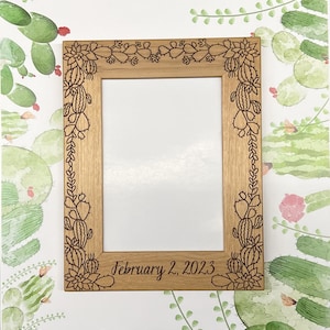 May include: A wooden picture frame with a cactus design and the date "February 2, 2023" engraved on the bottom.