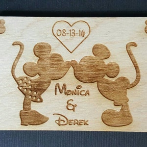 May include: A wooden sign with a Mickey Mouse and Minnie Mouse silhouette kissing. The sign has the date 08-13-16 and the names Monica & Derek.