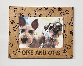 May include: A wooden picture frame with a brown wood finish and a bone and paw print design. The frame has a photo of two dogs, one brown and one gray, with the text "Opie and Otis" below the photo.