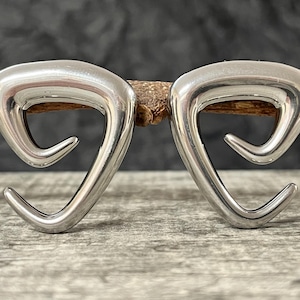 May include: A pair of silver-toned earrings featuring a smooth, polished, triangular spiral design. Each earring has an open, curved shape with a pointed end that curls inward, creating a continuous, fluid metallic form with a reflective surface.