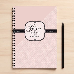 Può includere: Un quaderno a spirale rosa con un designo in bianco e nero. La copertina presenta il testo "Sugar Cakes & Cookies" e le parole "Sweet Dreams".