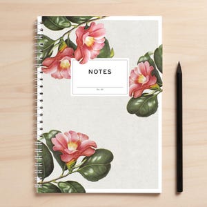 May include: A spiral bound notebook with a white cover featuring a floral design of pink camellia flowers and green leaves. The cover has the word "NOTES" printed in black text with the number "02" below it.