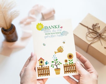 May include: A white card with a colorful illustration of a sunflower, a birdhouse, a watering can, and a small tree. The text on the card reads "DANKE dass du mir beim WACHEN geholfen hast".