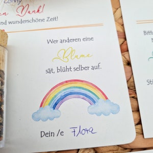K&ouml;nnte beinhalten: Eine wei&szlig;e Karte mit einem Regenbogen, Wolken und dem Text "Wer anderen eine Blume s&auml;t, bl&uuml;ht selber auf." Die Karte enth&auml;lt auch den Text "Dein/e Flora" und "Liebe/r Ju".