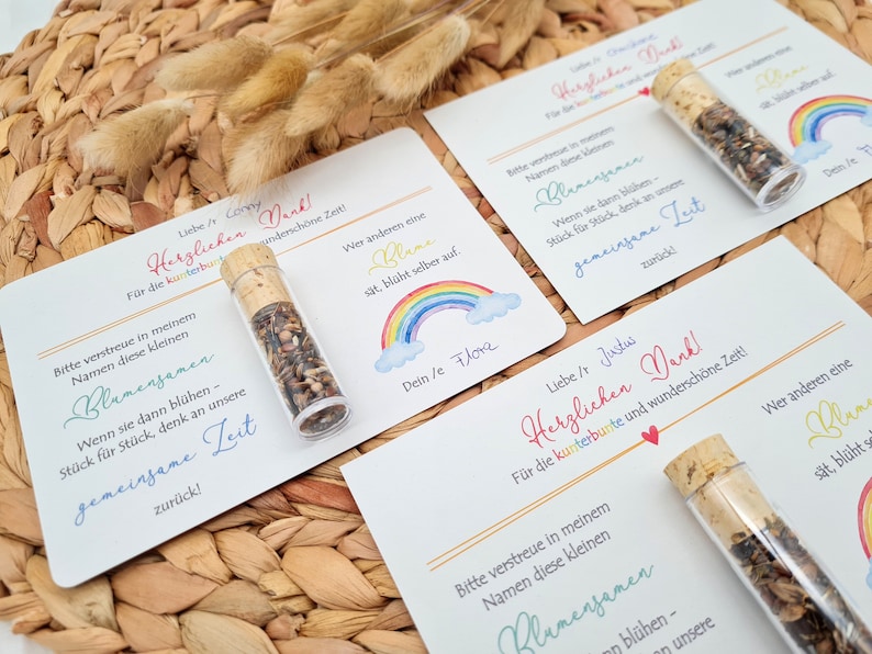 K&ouml;nnte beinhalten: Zwei wei&szlig;e Karten mit buntem Text und einer Regenbogen-Illustration. Der Text auf den Karten lautet "Herzlichen Dank!" was im Deutschen "Vielen Dank!" bedeutet. Jede Karte hat ein kleines Glasfl&auml;schchen mit Blumensamen. Die Fl&auml;schchen haben Korkstopfen.