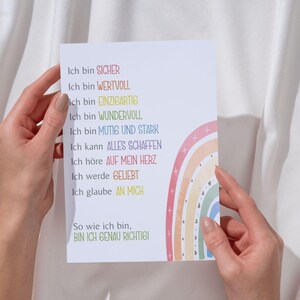 May include: A white card with a rainbow design and the text "Ich bin SICHER, Ich bin WERTVOLL, ich bin EINZIGARTIG, Ich bin WUNDERVOLL, Ich bin MUTIG UND STARK, Ich kann ALLES SCHAFFEN, Ich h&ouml;re AUF MEIN HERZ, Ich werde GELIEBT, Ich glaube AN MICH, So wie ich bin, BIN ICH GENAU RICHTIGI" in German.