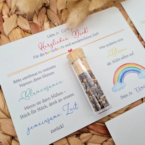 K&ouml;nnte beinhalten: Eine wei&szlig;e Karte mit einem Regenbogen-Design und dem Text "Wer anderen eine Blane s&auml;t, bl&uuml;ht selber auf." Die Karte enth&auml;lt auch den Text "Liebe / Corn Herzlichen Dank F&uuml;r die kunterbunte und wundersch&ouml;ne Zeit!" und "Dein le Flota". Ein kleines Glasfl&auml;schchen gef&uuml;llt mit Blumensamen befindet sich auf der Karte.