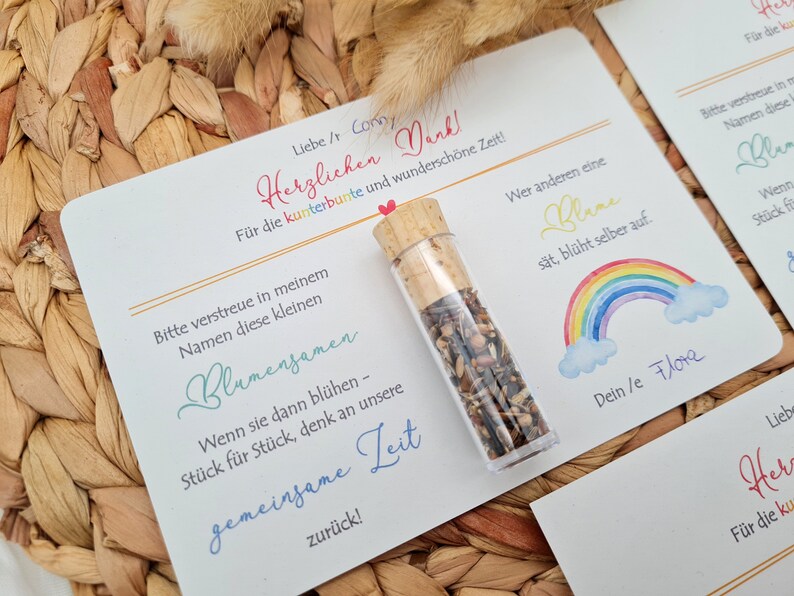 K&ouml;nnte beinhalten: Eine wei&szlig;e Karte mit einem Regenbogen-Design und dem Text "Wer anderen eine Blane s&auml;t, bl&uuml;ht selber auf." Die Karte enth&auml;lt auch den Text "Liebe / Corn Herzlichen Dank F&uuml;r die kunterbunte und wundersch&ouml;ne Zeit!" und "Dein le Flota". Ein kleines Glasfl&auml;schchen gef&uuml;llt mit Blumensamen befindet sich auf der Karte.