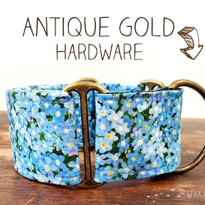 Puede incluir: Un collar de perro floral azul con herrajes de oro antiguo. El collar está hecho de tela con un patrón de pequeñas flores azules sobre un fondo blanco. Los herrajes son de metal y tienen un acabado brillante.