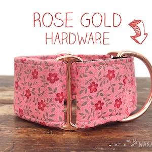 May include: A pink floral dog collar with rose gold hardware. The collar is made of fabric and has a floral pattern with small red flowers and green leaves. The hardware is made of rose gold metal and includes a buckle and a D-ring.