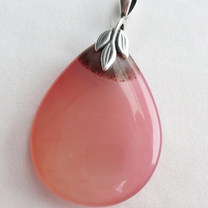 May include: A pink agate pendant with a silver leaf design. The pendant is teardrop shaped and has a smooth, polished finish.
