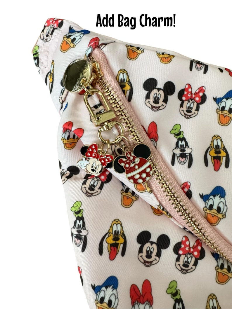 May include: A light pink cosmetic bag with a gold zipper and charm, featuring a pattern of Mickey Mouse, Minnie Mouse, Donald Duck, and Goofy. The bag has the text "Add Bag Charm!" in black.