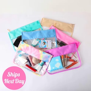 May include: Five clear zippered pouches with different colored fabric exteriors. The pouches are filled with various items, including makeup brushes, cosmetics, and a hairbrush. The pouches are a great way to organize your belongings.