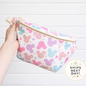 May include: A waist bag featuring a repeating pattern of pastel pink, purple, and blue mouse-ear silhouettes on a white background. The bag includes a gold-toned zipper closure and an adjustable strap. A circular badge displays the text SHIPS NEXT DAY.