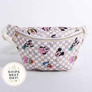 May include: A beige and white checkered fanny pack featuring a repeating pattern of cartoon character faces including Mickey Mouse, Minnie Mouse, Pluto, Donald Duck, and Daisy Duck, with a gold-toned zipper closure and an adjustable white strap.