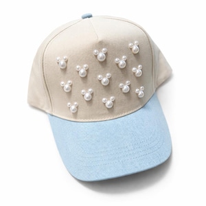 May include: A beige baseball cap with a light blue brim. The cap is decorated with multiple pearl-like embellishments arranged in a Mickey Mouse head shape.