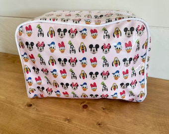 May include: A rectangular cosmetic bag with a light pink background featuring a repeating pattern of Disney character faces including Mickey Mouse, Minnie Mouse, Donald Duck, Daisy Duck, and Goofy, finished with white piping along the edges.