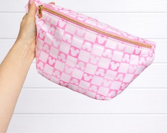 May include: A pink and white checkered fanny pack featuring a repeating pattern of mouse head silhouettes. The bag has a gold-toned metal zipper closure along the top edge and is constructed from a smooth, lightweight material.