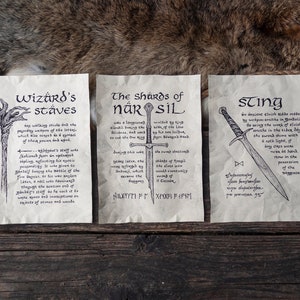 Op de afbeelding: Drie perkamenten rollen met illustraties en tekst over fantasiewapens. De rollen zijn getiteld "Wizard's Staves", "The Shards of Narsil" en "Sting".