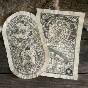 Op de afbeelding: Twee antieke hemelkaarten met ingewikkelde illustraties van dierenriemtekens, planeten en sterrenbeelden. De kaarten zijn gedrukt op verouderd papier, met een vintage esthetiek. De achtergrond is een rustiek houten oppervlak.