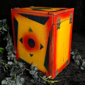 May include: A wooden box with a red, yellow, and black geometric design. The box has metal hinges and is closed.