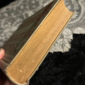 Peut inclure: Un livre ancien avec une couverture beige et des motifs d&eacute;coratifs rouges. Les pages sont jaunies, et la tranche montre des signes d'usure. Les bords du livre sont l&eacute;g&egrave;rement us&eacute;s, t&eacute;moignant de son &acirc;ge et de son utilisation.