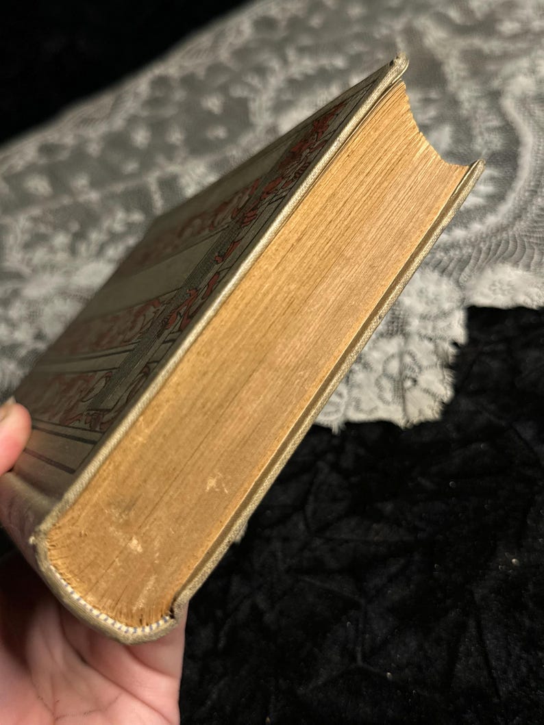 Peut inclure: Un livre ancien avec une couverture beige et des motifs d&eacute;coratifs rouges. Les pages sont jaunies, et la tranche montre des signes d'usure. Les bords du livre sont l&eacute;g&egrave;rement us&eacute;s, t&eacute;moignant de son &acirc;ge et de son utilisation.