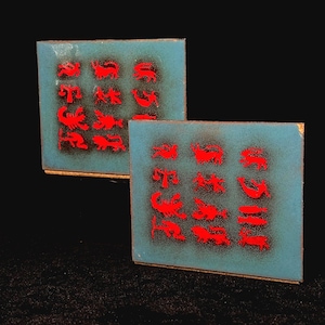 May include: Two square coasters with a turquoise background and red zodiac symbols. The coasters have a gold trim and are arranged side by side against a black background. Each coaster features twelve zodiac signs.