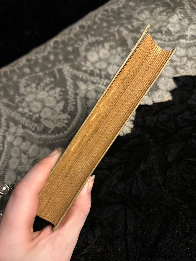 Peut inclure: Un livre ancien avec des pages jaunies et une tranche de couleur claire. La tranche du livre r&eacute;v&egrave;le le papier vieilli. Le livre est tenu en biais, soulignant son &eacute;tat usag&eacute; et son esth&eacute;tique vintage.