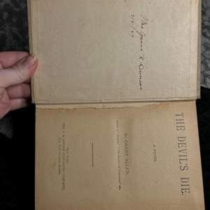 Peut inclure: Livre ancien ouvert, intitul&eacute; "THE DEVIL'S DIE" par Grant Allen. Les pages int&eacute;rieures sont jaunies, avec du texte visible et une inscription manuscrite. Publi&eacute; par The F. M. Lupton Publishing Company, New York.