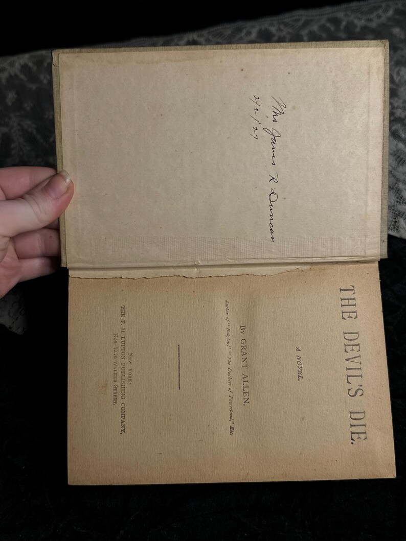 Peut inclure: Livre ancien ouvert, intitul&eacute; "THE DEVIL'S DIE" par Grant Allen. Les pages int&eacute;rieures sont jaunies, avec du texte visible et une inscription manuscrite. Publi&eacute; par The F. M. Lupton Publishing Company, New York.