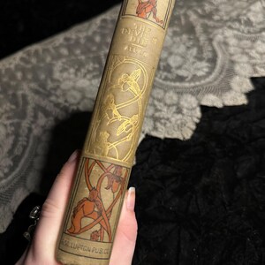 Peut inclure: Livre ancien intitul&eacute; "The Devil Dies" par Allen. Le livre a une couverture beige avec des &eacute;l&eacute;ments d&eacute;coratifs dor&eacute;s et orange. Le dos pr&eacute;sente le titre et le nom de l'auteur, avec une illustration d'une figure. Le nom de l'&eacute;diteur est imprim&eacute; en bas.