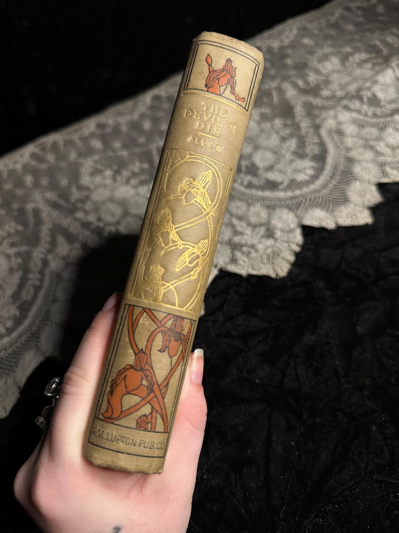 Peut inclure: Livre ancien intitul&eacute; "The Devil Dies" par Allen. Le livre a une couverture beige avec des &eacute;l&eacute;ments d&eacute;coratifs dor&eacute;s et orange. Le dos pr&eacute;sente le titre et le nom de l'auteur, avec une illustration d'une figure. Le nom de l'&eacute;diteur est imprim&eacute; en bas.
