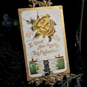 May include: Vintage Halloween postcard with a smiling pumpkin face bursting through a light blue background. The card features the text "To Greet You Heartily This Halloween" and a black cat. The card is displayed in a decorative gold frame.