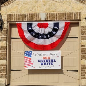 Welcome Home Soldier banner hung on a house exterior for a patriotic homecoming celebration. Banner includes name and rank, with American Flag motif