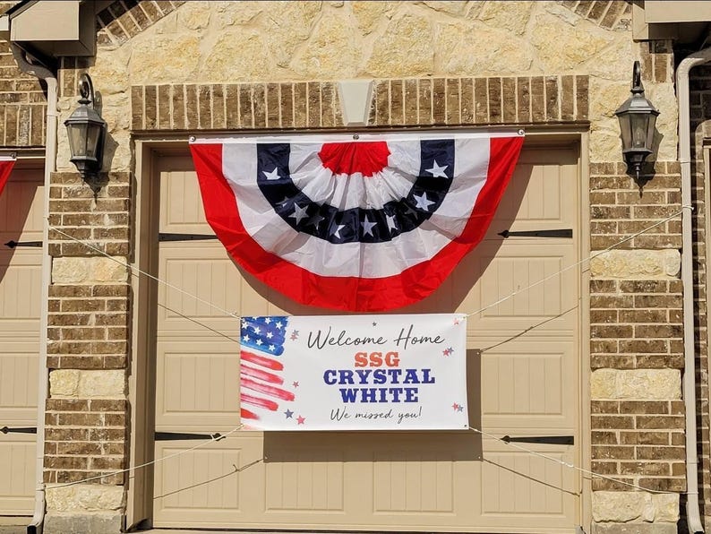 Welcome Home Soldier banner hung on a house exterior for a patriotic homecoming celebration. Banner includes name and rank, with American Flag motif