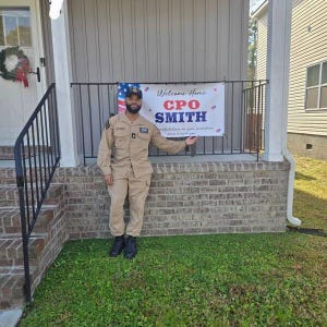 “Welcome Home” banner with stars, stripes, and bunting displayed on a brick home for a military welcome celebration.