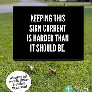 May include: A black sign with the text "KEEPING THIS SIGN CURRENT IS HARDER THAN IT SHOULD BE" in white lettering. The sign is on a metal frame in a grassy yard. A white circle with text is in the lower left.
