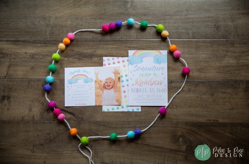 Puede incluir: Un juego de invitaciones de cumplea&ntilde;os con tem&aacute;tica de arco&iacute;ris. El juego incluye una tarjeta con una foto de un ni&ntilde;o, una tarjeta de agradecimiento y una invitaci&oacute;n que dice "Somewhere over the Rainbow, Aubrie is Two". Una guirnalda de bolas de fieltro coloridas rodea las tarjetas.