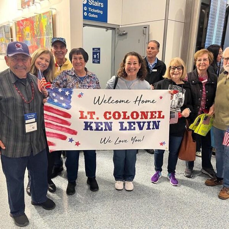 Group of friends and family celebrating with personalized “Welcome Home” banner at Honor Flight