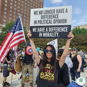 Protest Sign held by activist with social justice message that reads "We no longer have a difference in political opinion, we have a difference in morality" in black and white design with American flag in the background