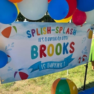 Splish Splash birthday banner for kids with rainbow primary colors, watercolor beach balls, life rings, and water splash accents